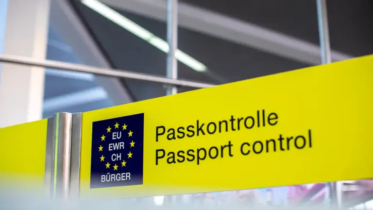 Dzeltena norāde lidostā ar uzrakstu Pasu kontrole un Eiropas Savienības simboliku.