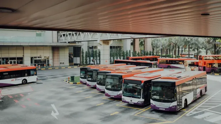 Vairāki pilsētas autobusi stāv autoostas laukumā, gaidot savu nākamo reisu izbraukšanai.