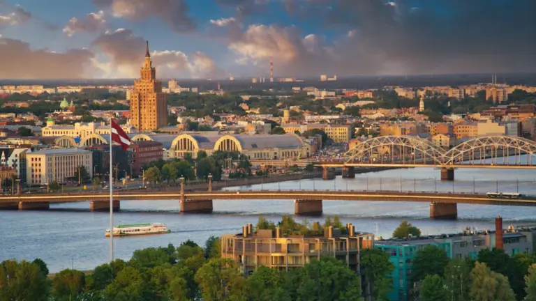 Panorāmas skats uz Rīgas vecpilsētu un Daugavas upi saulainā vasaras vakarā.