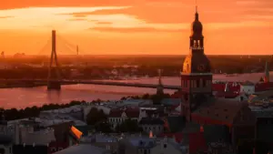 Panorāmas skats uz Rīgas siluetu, Vanšu tiltu un Daugavu vakara saulrietā.