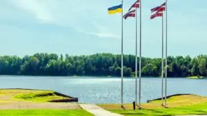 Latvijas un Ukrainas karogi plīvo pie mierīga ezera un zaļa meža