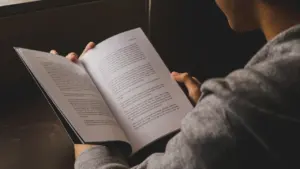 Cilvēks lasa atvērtu grāmatu ar tekstu mājīgā un mierīgā noskaņā.
