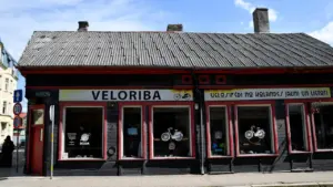 Vēsturiska koka ēka Liepājā ar velosipēdu veikala izkārtni uz ielas fona.