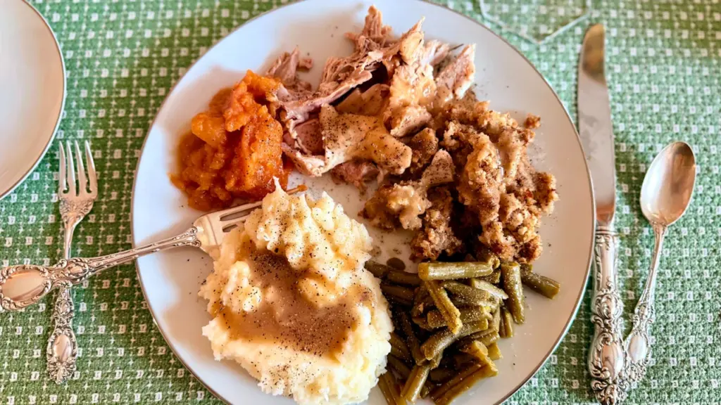 Šķīvis ar tradicionālu svētku maltīti uz zaļa galdauta Miķeļdienas ražas svētku noskaņās.